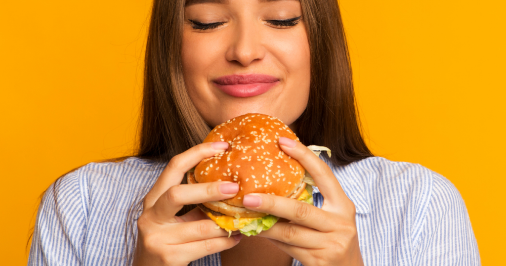 woman eating a hamburger happily, not dieting